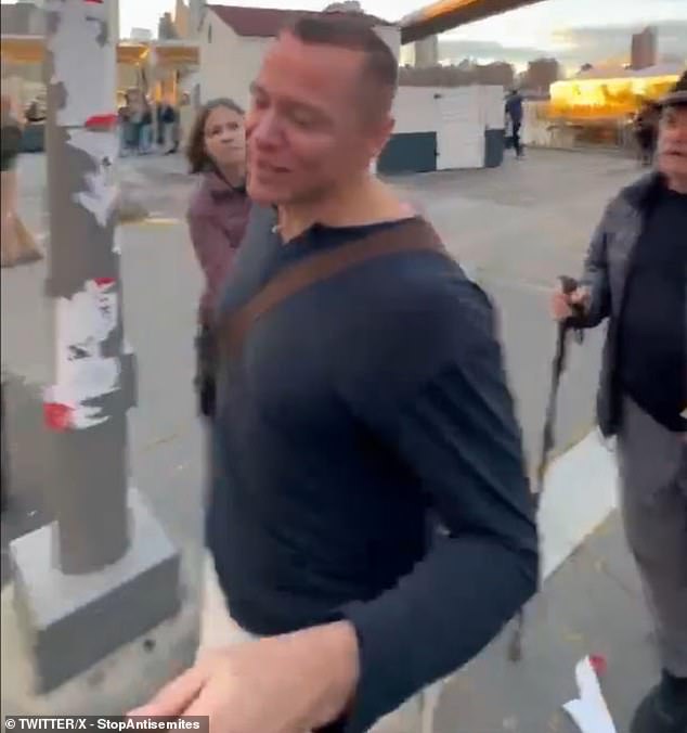 A man in a blue shirt grins at her and tries to cover the camera with one hand before walking past