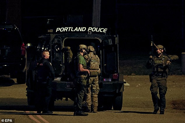 Police officers surround an armored law enforcement vehicle parked in the parking lot of the high school gymnasium in Lisbon