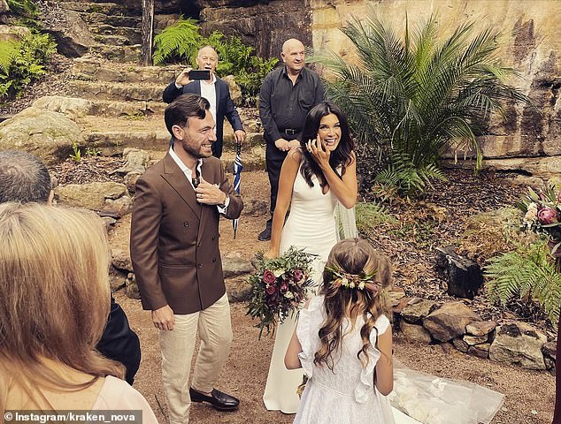 Amelia wore a simple sleeveless white wedding dress with a plunging neckline that fell all the way to the floor.  Adam wore a brown double-breasted blazer