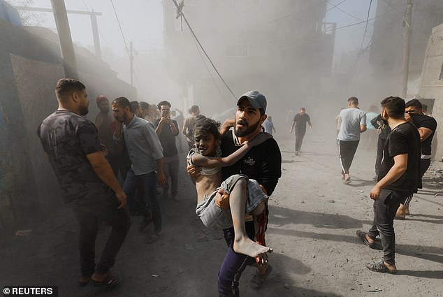 A Palestinian man carries a child victim at the scene of Israeli attacks on homes