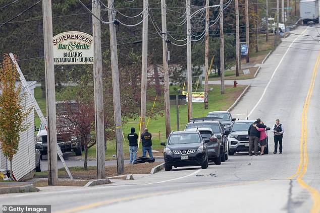 A woman hugs a law enforcement officer as they investigate outside the scene of a mass shooting at Schemengees Bar and Grille