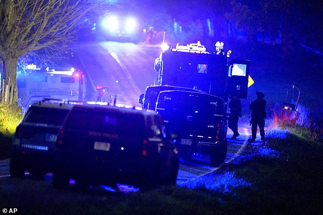 Law enforcement officers, right, stand next to armored and tactical vehicles, center, near a property on Meadow Road, in Bowdoin, Maine, Thursday evening