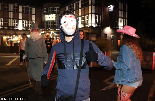 A man dressed as Michael Myers from the 1979 Halloween film with a wizard and a cowgirl in the background