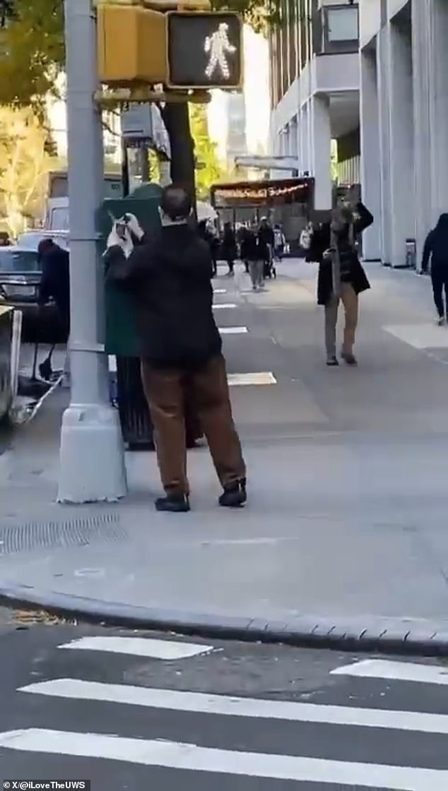 In the video, Simon, wearing a black jacket and brown pants, begins cutting the posters depicting the Israeli hostages and pulls them down.