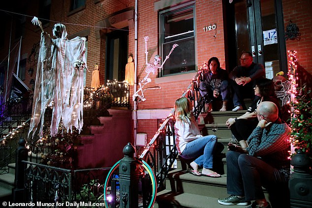 Brave residents of a New Jersey neighborhood sat on the steps of a brownstone house, engaged in casual conversation, seemingly undisturbed by the ghost in tattered white clothes staring at them from behind