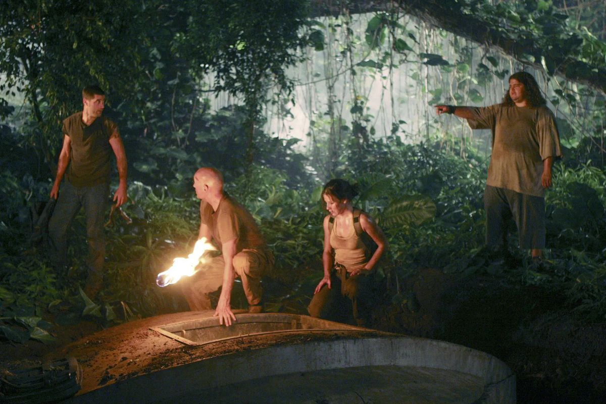 Matthew Fox, Terry O'Quinn, Evangeline Lilly, and Jorge Garcia standing in front of a concrete hearth surrounded by a tropical forest in Lost.