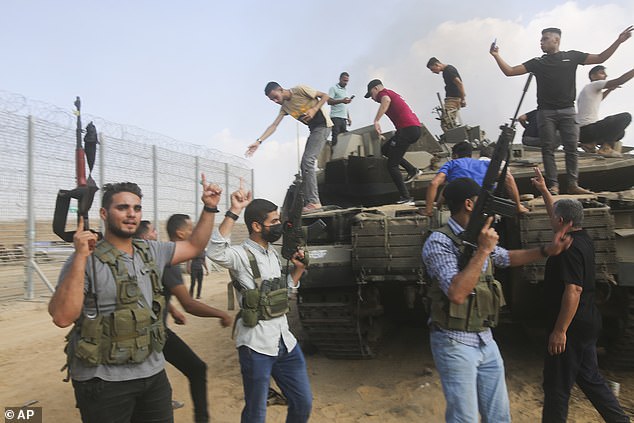 Palestinian militants celebrate near an Israeli tank at the Gaza Strip border fence on October 7.  More than 1,400 Israelis were killed