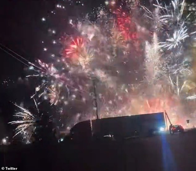 The silhouette of the massive semi-truck can be seen as fireworks shoot into the night sky