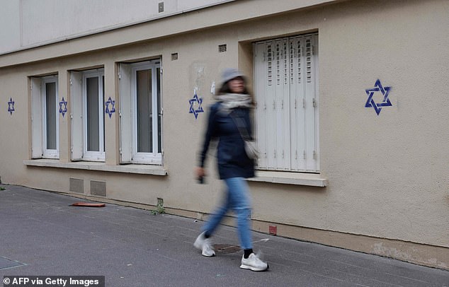 In the 14th arrondissement of Paris, approximately sixty blue stars were found graffitied on various buildings during the night.  Pictured: A woman walks past a building marked with stars