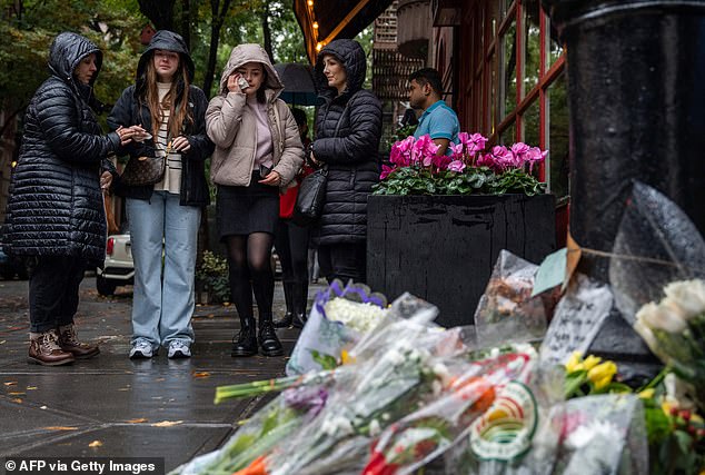 People stand for floral tributes to actor Matthew Perry outside the apartment complex used as an exterior shot in the TV show Friends in New York on Sunday