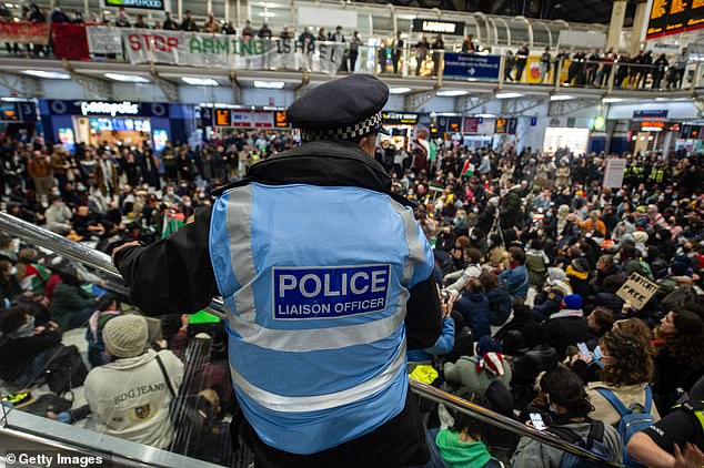 A police officer watches as protesters sit on the floor of Liverpool Street station