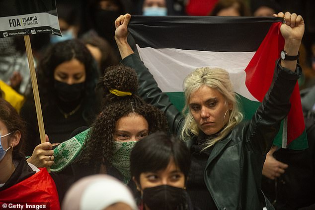 A woman is pictured holding up the Palestinian flag at London station