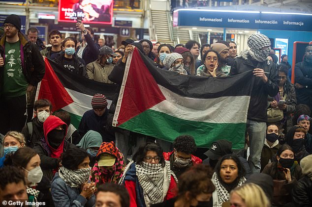 Protesters wearing masks and scarves are shown holding up the Palestinian flag