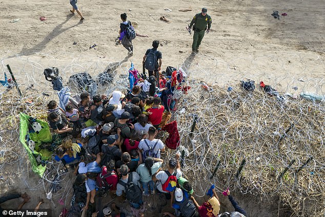 A U.S. Border Patrol agent monitors as immigrants enter the United States after crossing the Rio Grande from Mexico in Eagle Pass, Texas, on September 30, 2023.  The officer had cut rolls of barbed wire to allow them to pass through for processing