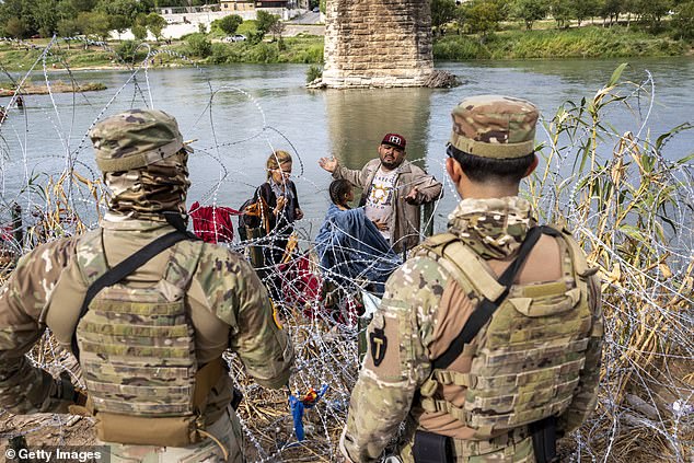 Texas National Guard troops watch as migrants cross the Rio Grande River from Mexico on September 27