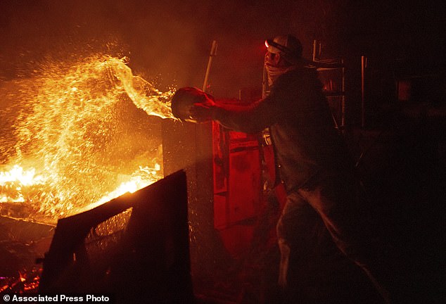 California resident Francis Lopez extinguishes flames with a bucket of water as a wildfire called Highland Fire burns through his property in Aguanga, California