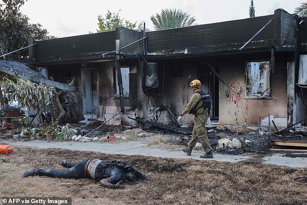 An Israeli soldier walks past a dead Palestinian fighter as troops investigate the scene of an attack on the Israeli kibbutz of Kfar Aza on the border with the Gaza Strip