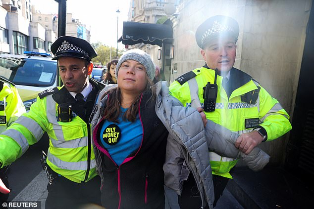 Greta Thunberg, wearing a large badge reading 'Oily Money Out', is led away from the Intercontinental Hotel Park Lane by two Met police officers