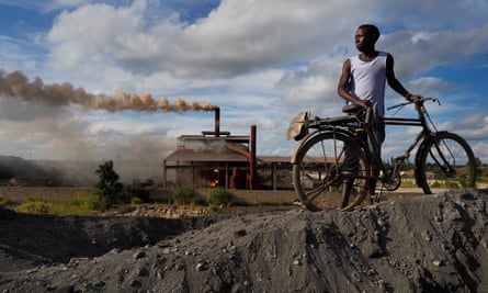 A man with a bicycle rack on a pile of black lead with a smoking fire in the background