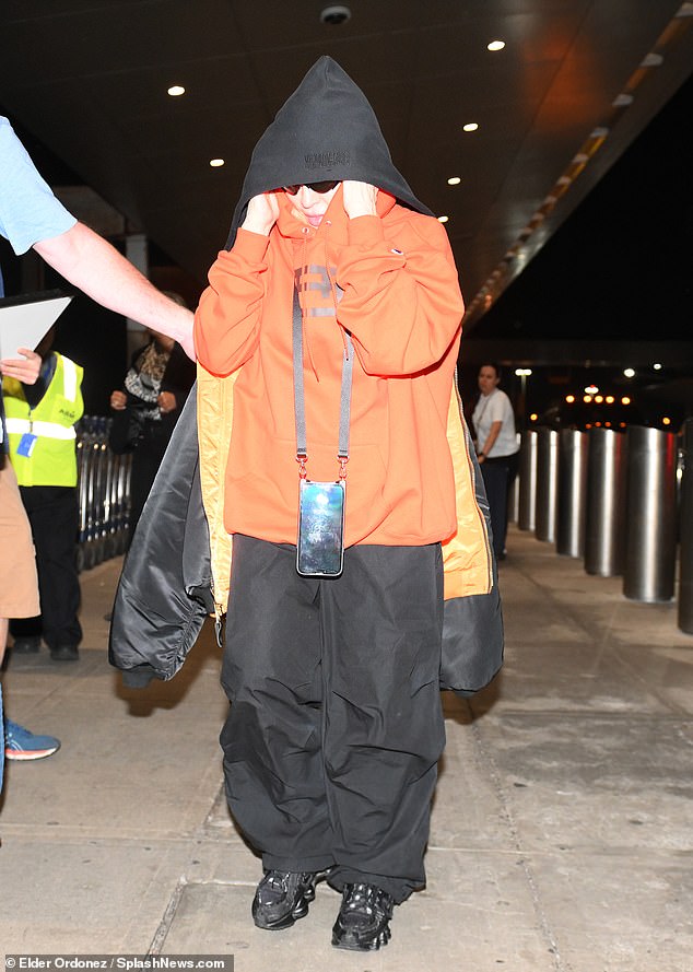 Seven-hour flight: Michigan native Madge - brandishing a lanyard for her iPhone - hid her 6-foot-2 figure under a baggy orange hoodie, black wide-leg sweatpants and matching sneakers