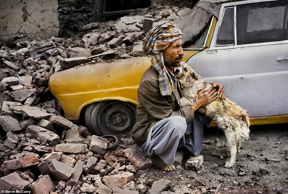 In Kabul, Afghanistan, a man is seen hugging his dog next to his taxi, which was destroyed when the nearby building collapsed during shelling.  The emotional photo was taken by McCurry in 1992