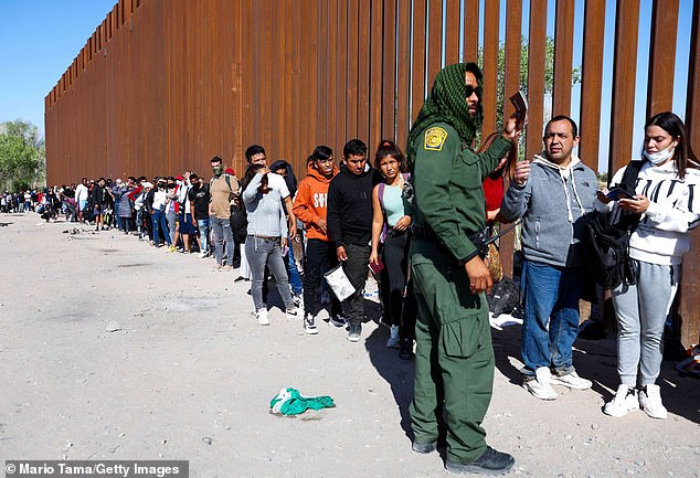 A U.S. Border Patrol agent checks the identification of immigrants as they wait in line for processing after crossing from Mexico in Yuma, Ariz., May 21, 2022