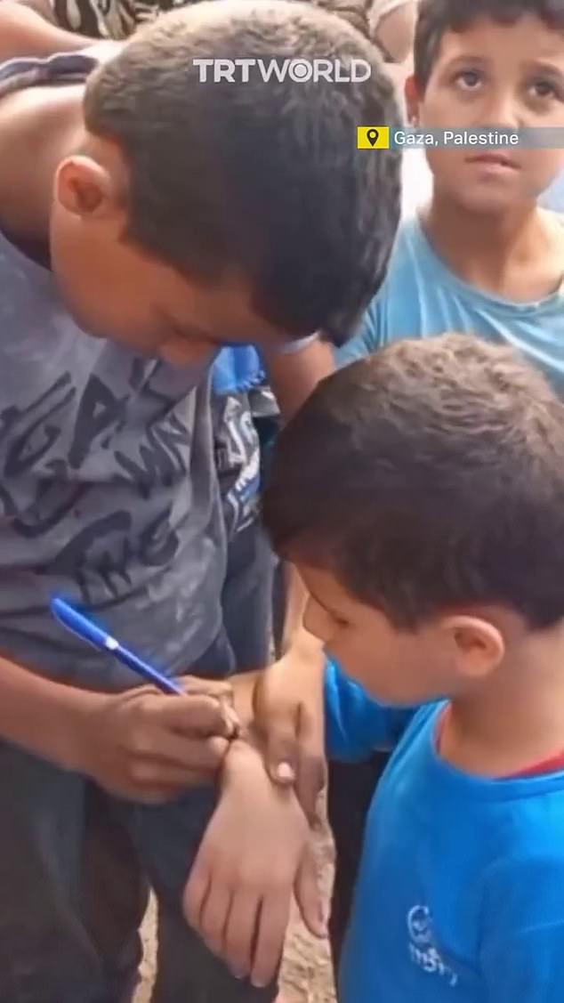 Desperate: A boy helps his friend by writing his name on his arm in Gaza so their bodies can be identified if they die in airstrikes
