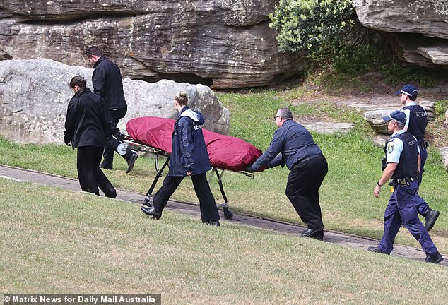 Paul Thijssen's body is wheeled to a mortuary van after being recovered from the rocks beneath the Diamond Bay Reserve on Friday afternoon