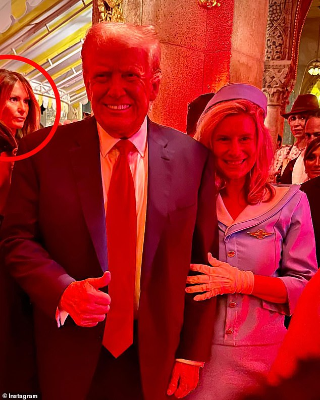 Melania Trump is seen standing behind Donald Trump as he poses for a photo with a partygoer