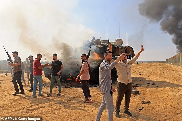 Hamas terrorists are pictured taking selfies in front of a burning Israeli tank near the Gaza border wall on October 7