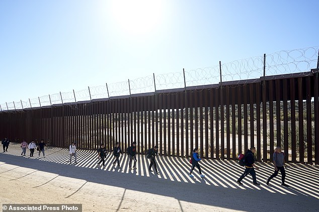 A group of people, including many from China, walk along the wall after crossing the border with Mexico to seek asylum, Oct. 24 near Jacumba, California