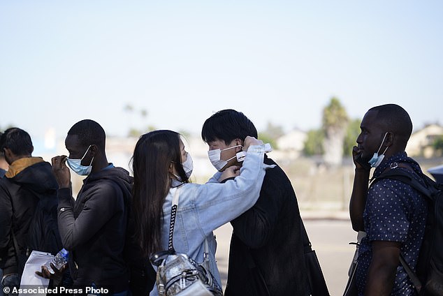 A couple from China adjusts their masks as they wait to board a bus to the airport after crossing the border and being dropped off by Border Patrol agents at a transit center in San Diego