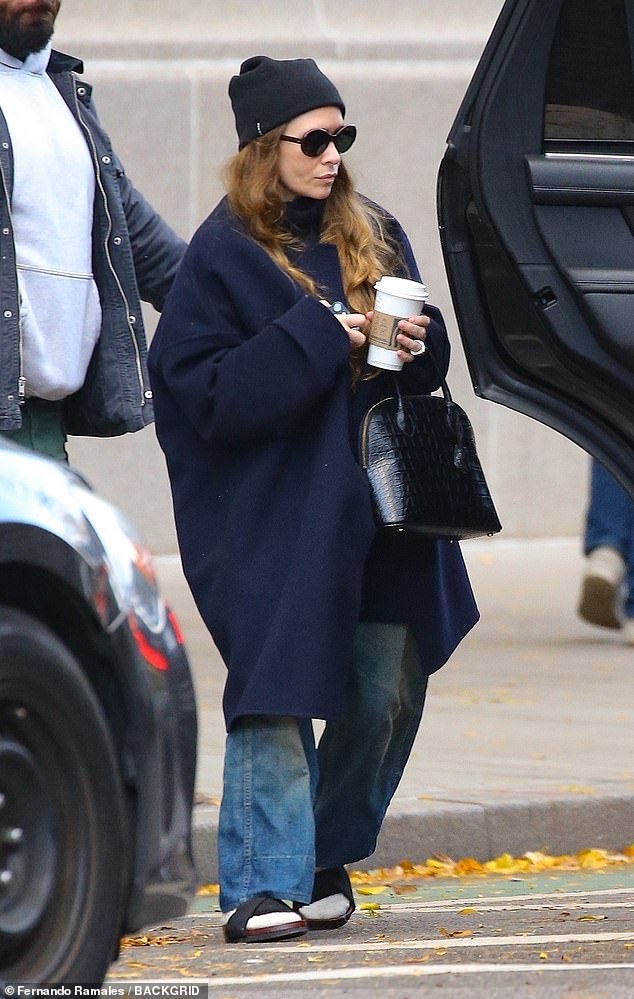 Full hands: The fashion designer wore an oversized navy blue coat while holding a coffee cup and carrying a black textured leather bag