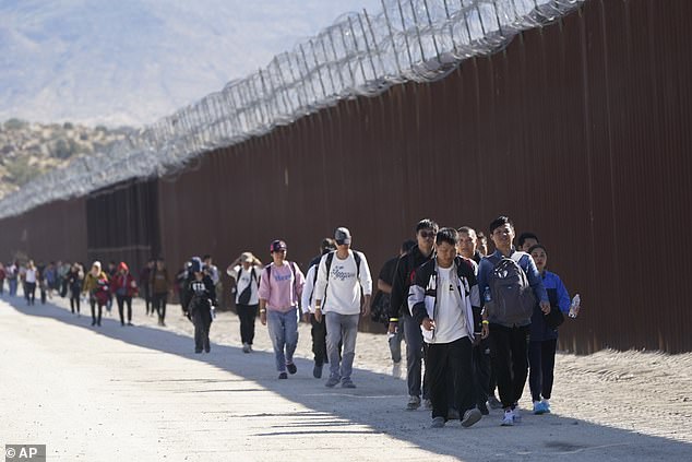 A group of migrants pictured walking along the US-Mexico border wall as immigration numbers continue to set records, including a total of 269,735 border patrol officers in September