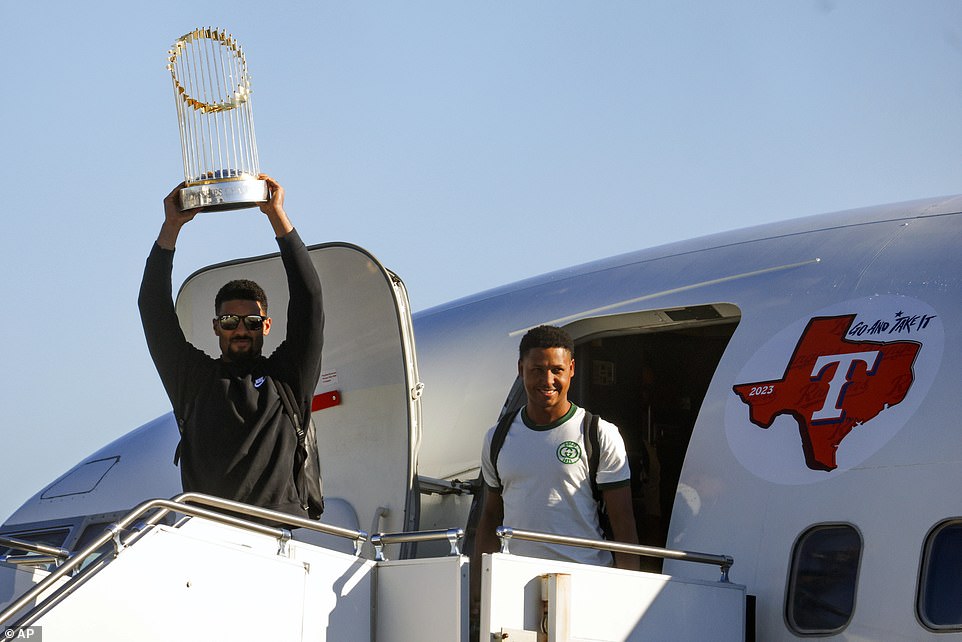 Rangers' Marcus Semien (L) hoists the Commissioner's Trophy alongside pitcher Jose Leclerc (R) upon their arrival at Dallas Love Field on Thursday