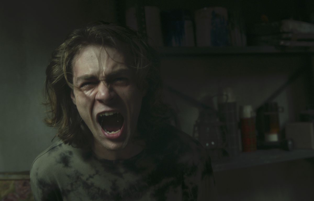 Insidious series regular character Dalton (Ty Simpkins), now grown into a shaggy-haired teenager, screams in a dark, gloomy room in Insidious: The Red Door