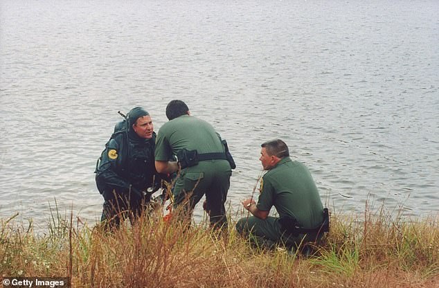 Law enforcement officers, 1 dressed in scuba gear, talk along the lakeshore as they comb the water bottom looking for the car of Susan Smith, who admitted to drowning her sons in John D. Long Lake