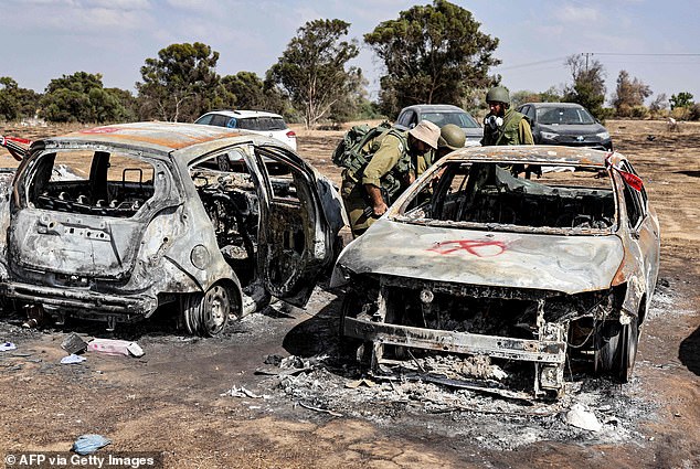 Israeli Army soldiers search the remains of a torched vehicle for forensic evidence at the scene of the October 7 attack on the Supernova Desert Music Festival