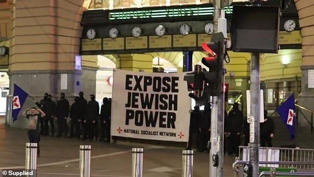 Neo-Nazis in Melbourne hold up an anti-Semitic banner before marching through Flinders St Station giving the now banned Hitler salute