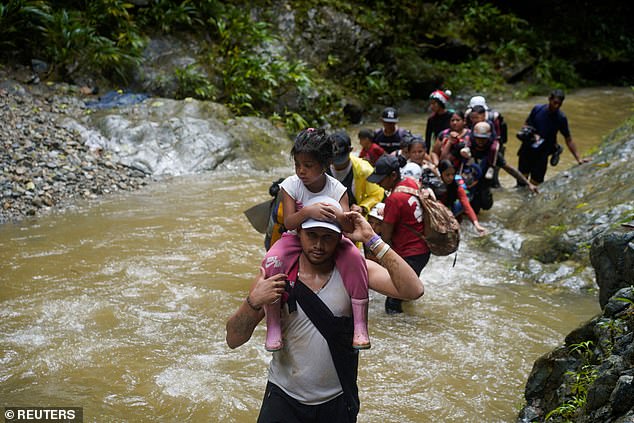 The US is also experiencing a major increase in arrivals via a dangerous route through Panama's Darién Gap jungle – a stretch of jungle that connects Central America to the south.  Pictured: A migrant carrying a child as they traverse the route during their journey to the US in July