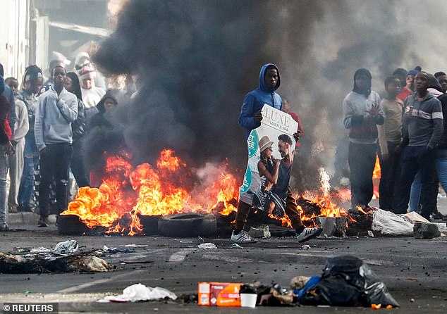 The deaths come amid violence across Cape Town in response to police confiscating illegal vehicles.  In the photo: Residents of Masiphumelele gather near burning tires during protests