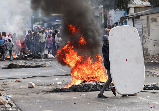 A Masiphumelele resident uses a sign as a shield during clashes with law enforcement agencies amid an ongoing strike by taxi companies against traffic authorities in Cape Town, August 8