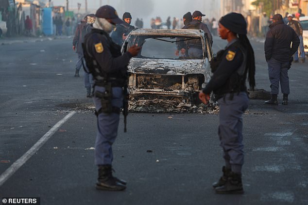 Members of the South African Police Service stand near a burnt-out vehicle in Nyanga during the ongoing taxi operators' strike in Cape Town, South Africa, August 7, 2023