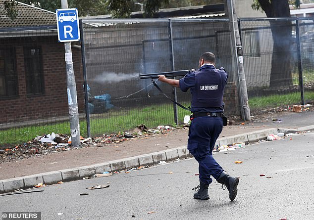 A law enforcement officer fires rubber bullets during their clashes with protesters in Masiphumelele, amid an ongoing strike by taxi companies