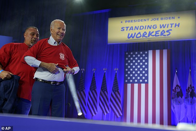 Matt Frantzen, president of UAW Local 1268, helps Biden put on the T-shirt