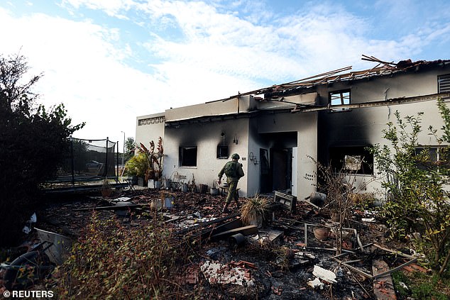 An Israeli soldier walks towards the remains of a burned house, after a deadly infiltration by Hamas gunmen from the Gaza Strip, in Kibbutz Beeri