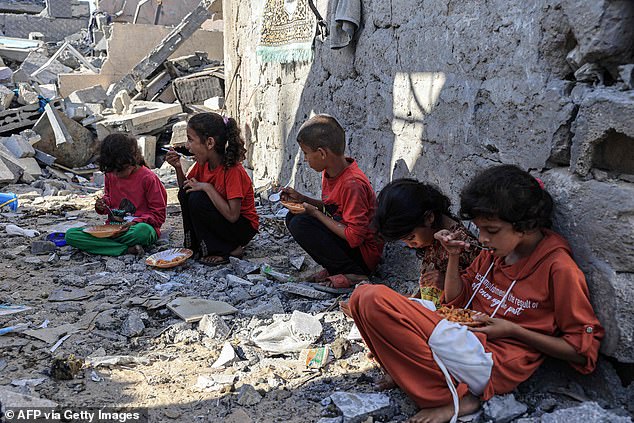 The children of Amal al-Robayaa eat their meals amid the ruins of the family home destroyed during an Israeli attack in Rafah in the southern Gaza Strip