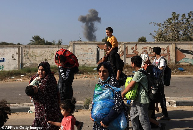 Smoke rises in the background as Palestinian families flee Gaza City and other parts of northern Gaza for southern areas