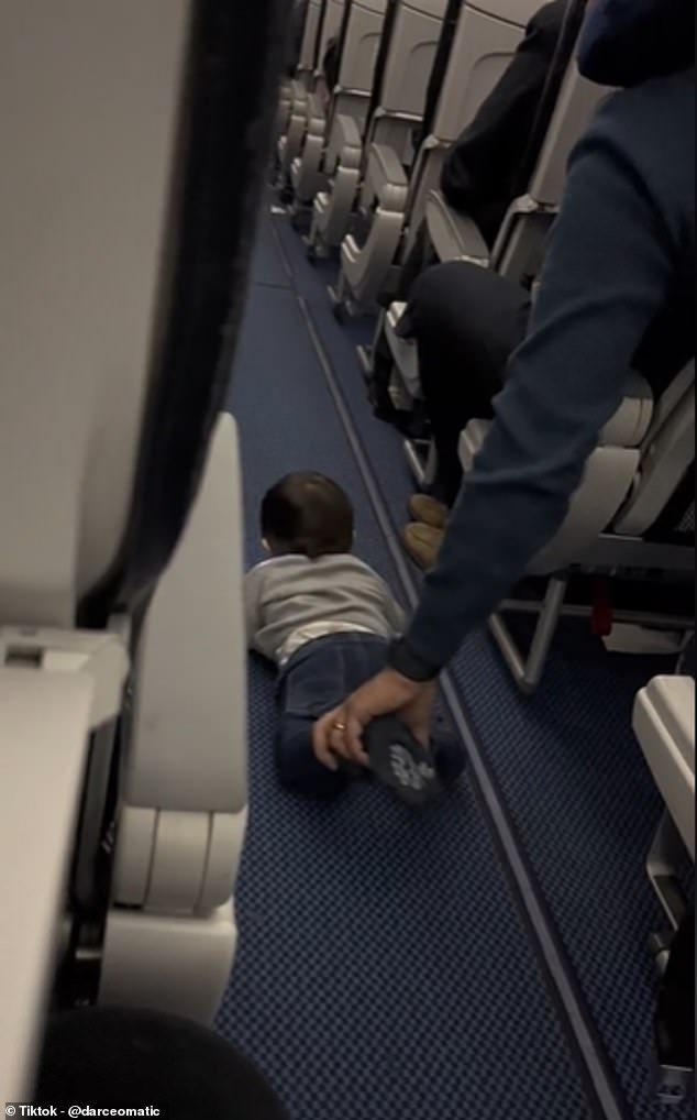 Dangling his left hand, the father lets the toddler crawl a distance down the empty aisle - before pulling him back to his seat by the pants so the child can climb back up the aisle