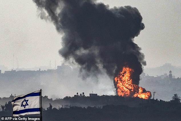 An Israeli flag flies over a position in southern Israel as it crosses the border into the Gaza Strip, and a fireball erupts during the Israeli bombardment on November 8